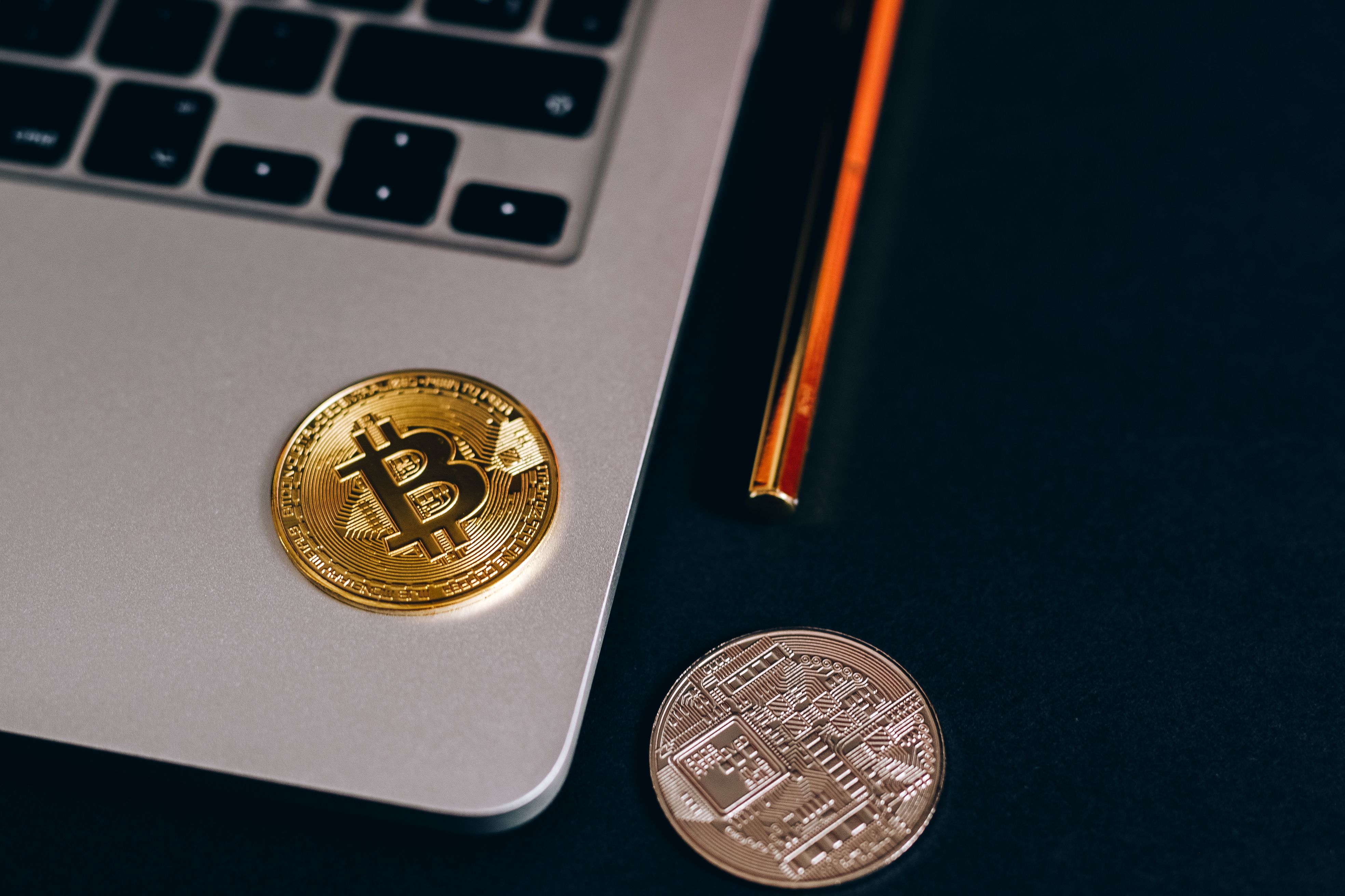 Gold Bitcoin coin resting on a laptop next to the keyboard and pencil