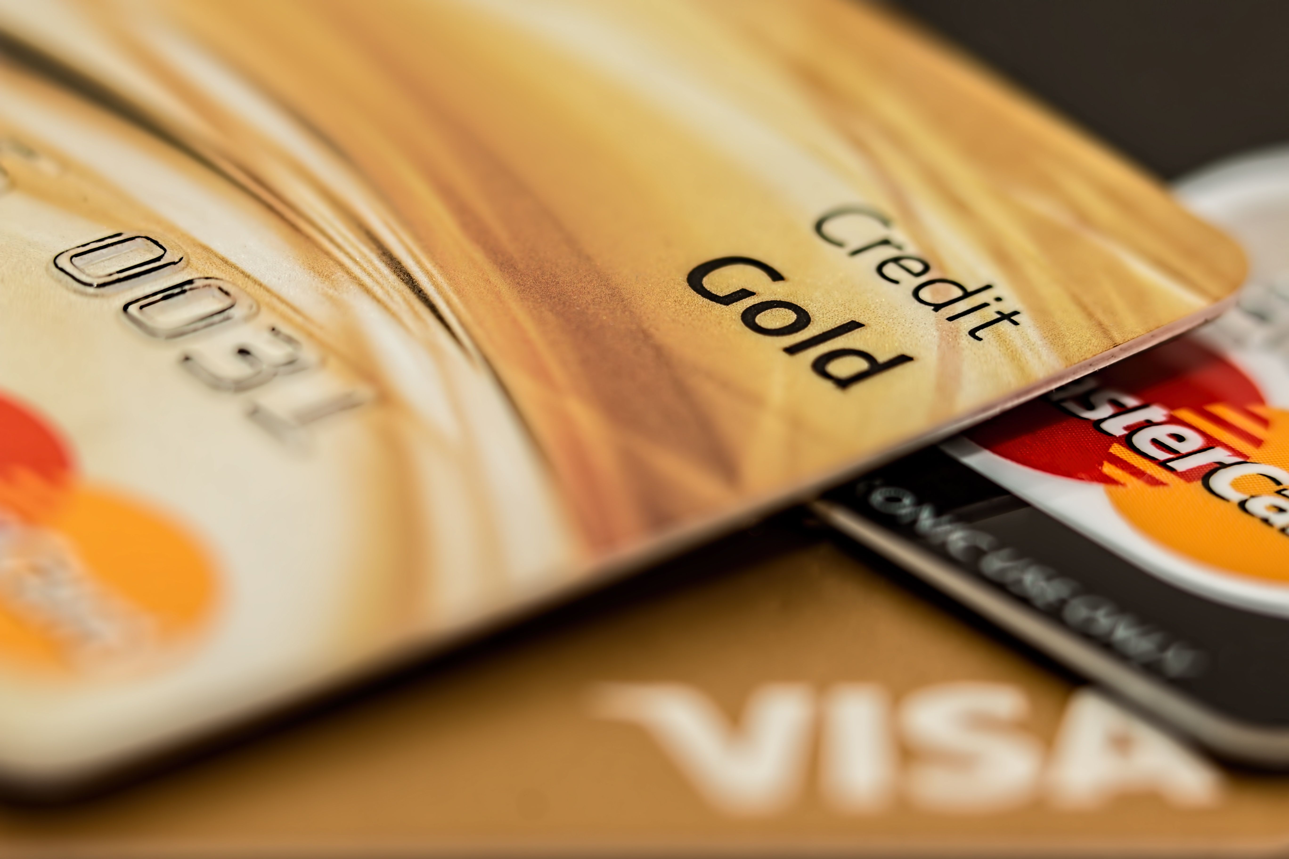 Close-up of a gold Mastercard credit card labelled “Credit Gold,” with embossed numbers, resting at an angle on a Mastercard and a gold Visa card, shot with shallow depth of field.